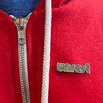 Unrest Metallic Enamel Pin on red sweatshirt